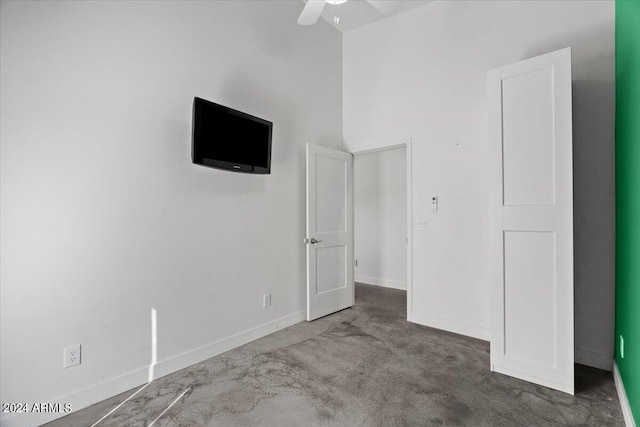 unfurnished bedroom featuring ceiling fan, a towering ceiling, and dark carpet