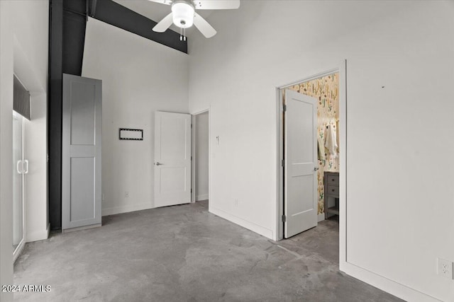 unfurnished bedroom with concrete floors, baseboards, a high ceiling, ensuite bath, and a ceiling fan