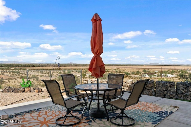 view of patio / terrace featuring a rural view, fence, outdoor dining space, and a mountain view