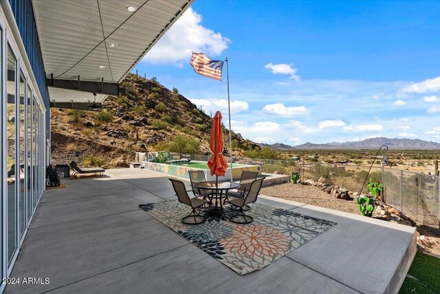 view of patio featuring outdoor dining area, a swimming pool, fence, and a mountain view