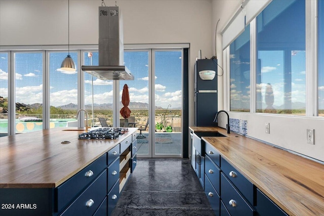 kitchen with sink, island exhaust hood, hanging light fixtures, butcher block countertops, and blue cabinetry