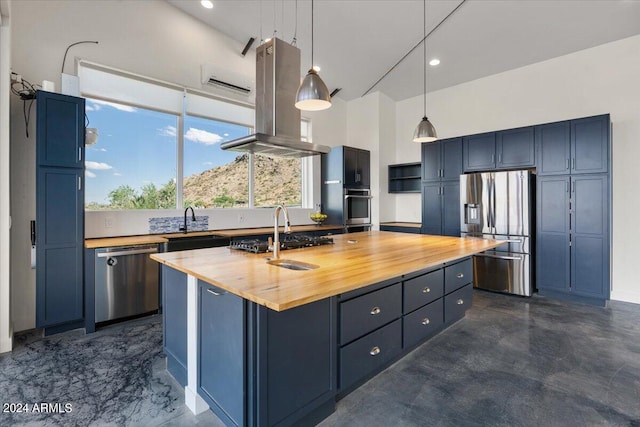 kitchen featuring appliances with stainless steel finishes, blue cabinets, butcher block countertops, island exhaust hood, and a kitchen island with sink