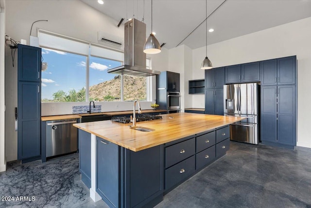 kitchen with butcher block counters, a center island with sink, appliances with stainless steel finishes, island range hood, and hanging light fixtures