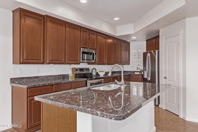 kitchen with dark stone counters, sink, an island with sink, and stainless steel appliances