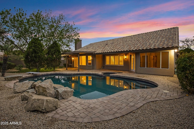 pool at dusk with an outdoor pool, a hot tub, a diving board, and a patio