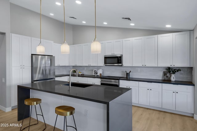 kitchen with light wood finished floors, visible vents, dark countertops, appliances with stainless steel finishes, and a sink