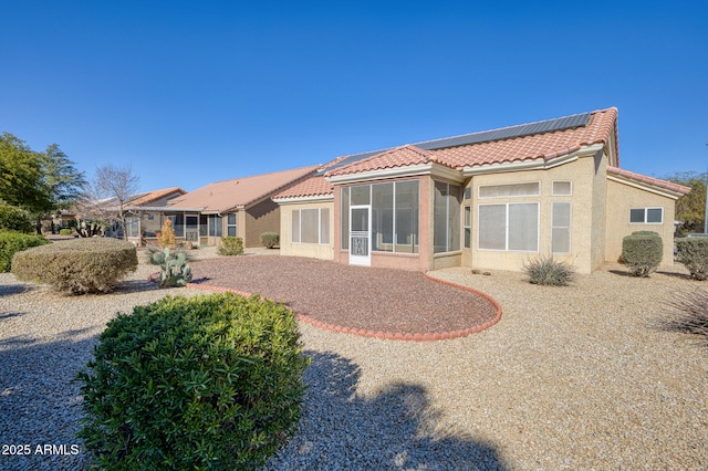 back of house featuring a sunroom and solar panels