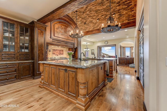 bar featuring light wood-style flooring, a sink, brick ceiling, hanging light fixtures, and a notable chandelier