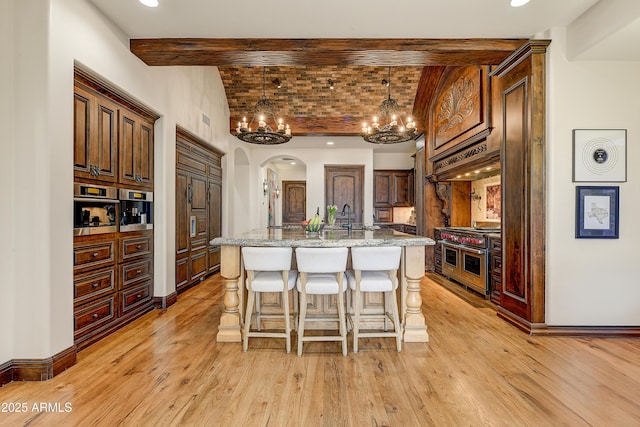 kitchen with appliances with stainless steel finishes, brick ceiling, light wood-type flooring, and a kitchen island with sink