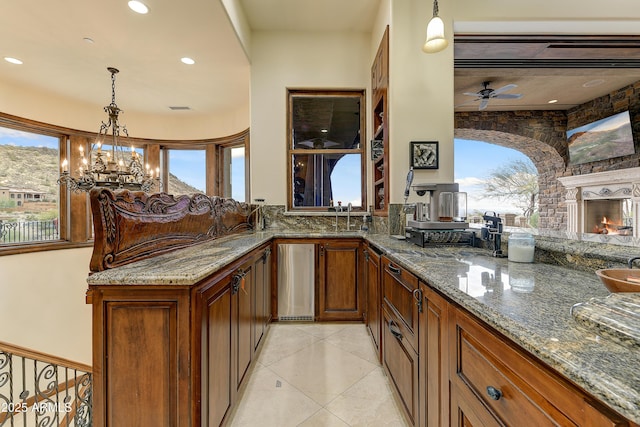 kitchen featuring light tile patterned floors, a fireplace, dark stone counters, and decorative light fixtures