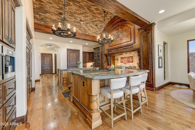 kitchen with baseboards, an island with sink, brick ceiling, light wood-style floors, and a kitchen bar