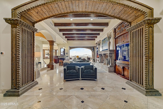 interior space with arched walkways, beam ceiling, a stone fireplace, and ornate columns