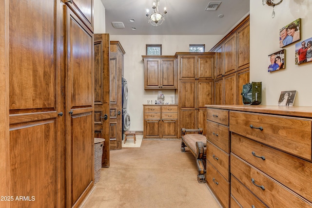 walk in closet with light carpet, an inviting chandelier, visible vents, and stacked washer and clothes dryer