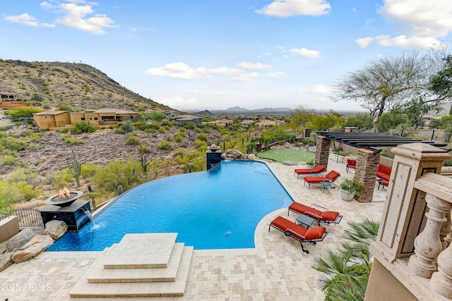 view of swimming pool with an infinity pool, a patio, fence, and a mountain view