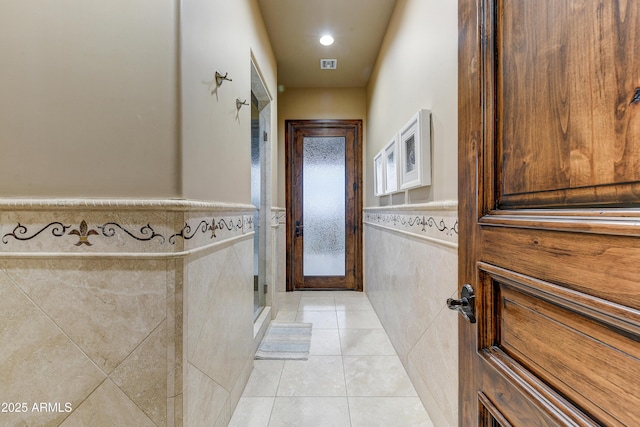 doorway to outside with light tile patterned floors, tile walls, and a wainscoted wall