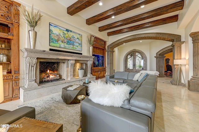 living room featuring arched walkways, recessed lighting, a premium fireplace, beamed ceiling, and ornate columns