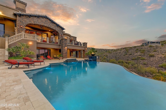 pool at dusk with an infinity pool and a patio