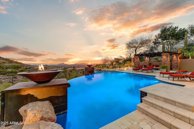 pool at dusk with a fire pit, a patio area, and an infinity pool