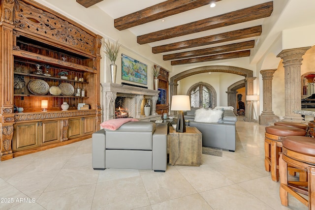 sitting room with arched walkways, beam ceiling, decorative columns, light tile patterned flooring, and a lit fireplace