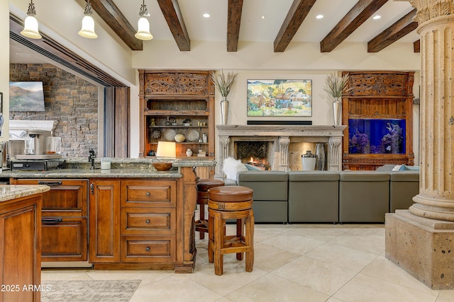 kitchen with brown cabinets, decorative columns, a premium fireplace, open floor plan, and light tile patterned flooring