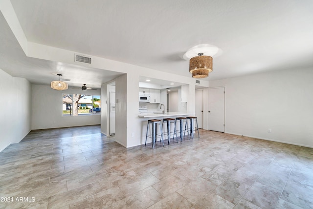 interior space featuring pendant lighting, a breakfast bar area, light countertops, open floor plan, and white cabinetry