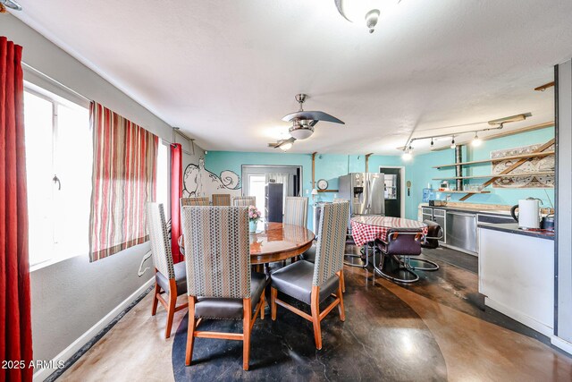 dining space featuring wet bar, a ceiling fan, baseboards, track lighting, and concrete flooring
