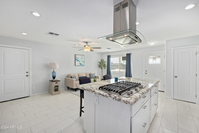 kitchen with ceiling fan, stainless steel gas cooktop, white cabinets, island range hood, and a center island