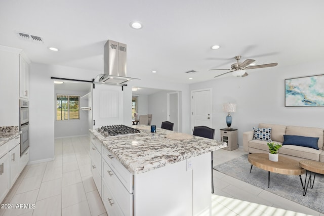 kitchen featuring a barn door, white cabinetry, island exhaust hood, light stone countertops, and ceiling fan