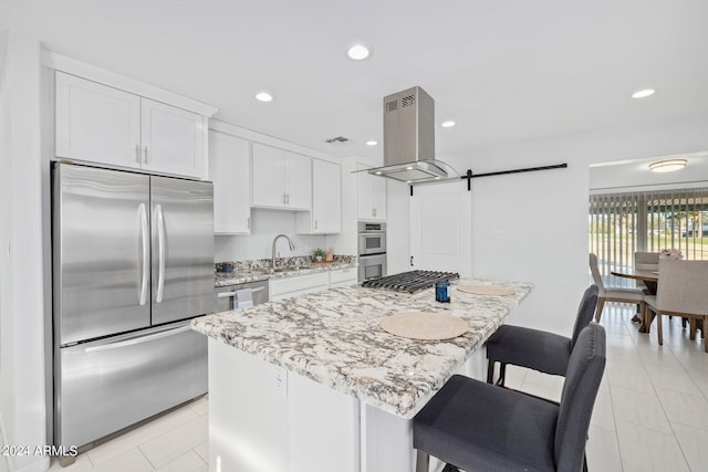 kitchen with island exhaust hood, stainless steel appliances, a barn door, white cabinetry, and a center island