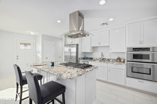 kitchen with stainless steel appliances, a center island, a breakfast bar, white cabinets, and island exhaust hood