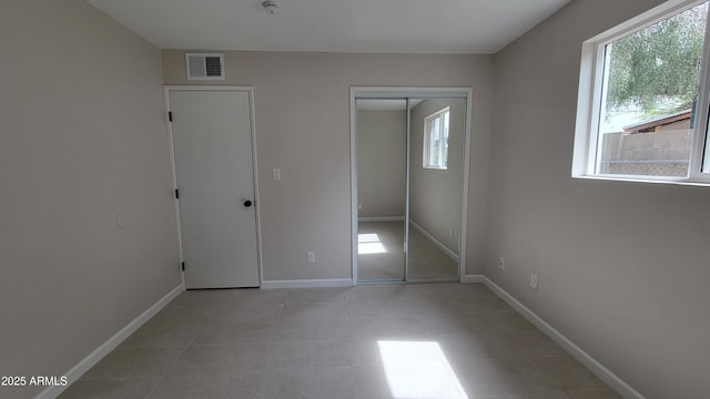 unfurnished bedroom featuring multiple windows, light tile patterned flooring, baseboards, and a closet