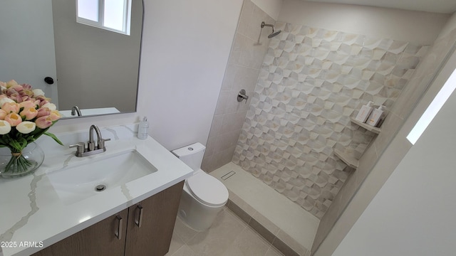 bathroom with toilet, a tile shower, vanity, and tile patterned flooring