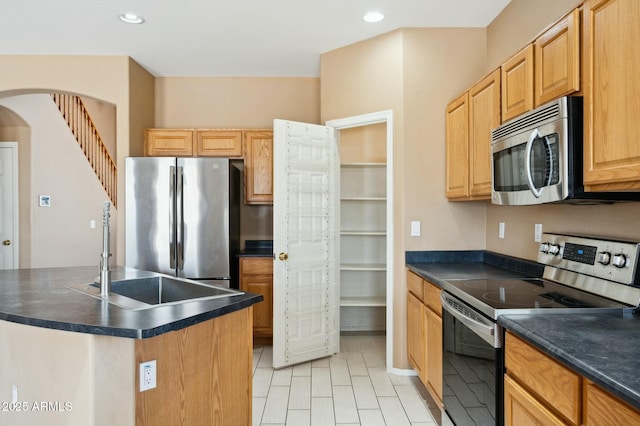 kitchen featuring stainless steel appliances, recessed lighting, dark countertops, an island with sink, and a sink