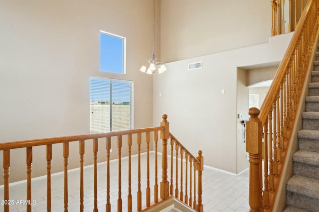 stairway with a high ceiling, baseboards, visible vents, and a chandelier