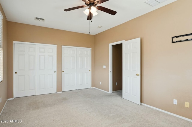 unfurnished bedroom with baseboards, carpet floors, visible vents, and two closets