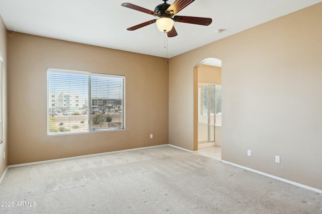 carpeted empty room featuring a ceiling fan, arched walkways, and baseboards