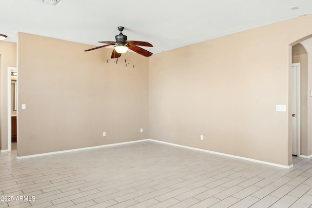 spare room featuring a ceiling fan, light wood finished floors, baseboards, visible vents, and arched walkways