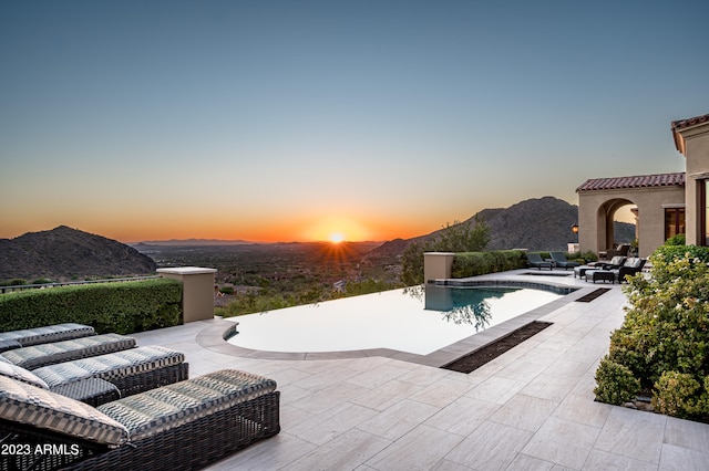 pool at dusk featuring a patio and a mountain view