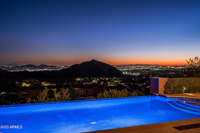 pool at dusk featuring a hot tub and a mountain view