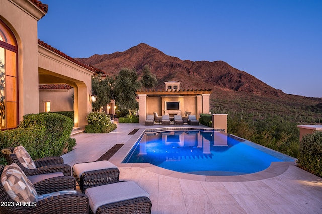 pool at dusk featuring a patio, a mountain view, and a fireplace