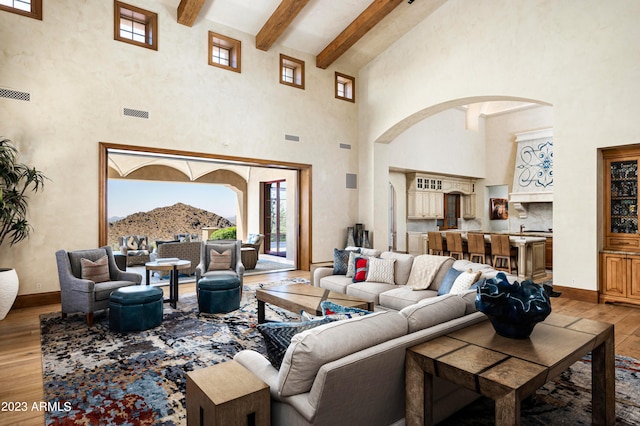 living room featuring light hardwood / wood-style flooring, beam ceiling, and a high ceiling