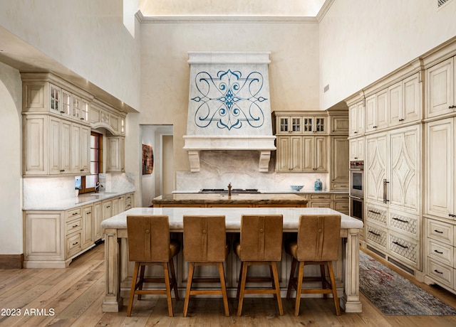 kitchen with a towering ceiling, light hardwood / wood-style flooring, cream cabinetry, and a kitchen island with sink