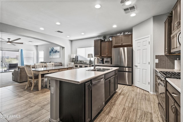 kitchen with sink, tasteful backsplash, dark brown cabinets, appliances with stainless steel finishes, and an island with sink