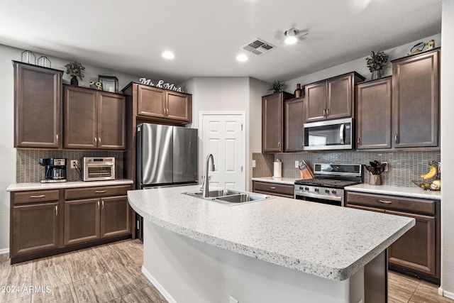 kitchen featuring an island with sink, stainless steel appliances, sink, and dark brown cabinetry