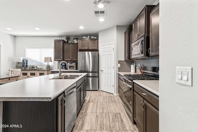 kitchen with sink, appliances with stainless steel finishes, tasteful backsplash, dark brown cabinetry, and a center island with sink