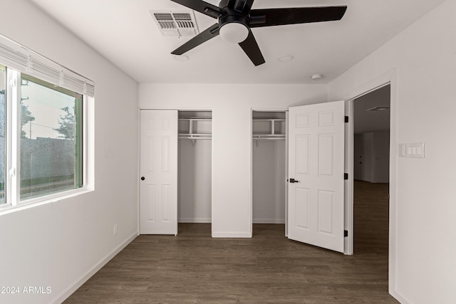 unfurnished bedroom featuring dark hardwood / wood-style flooring, ceiling fan, and multiple closets