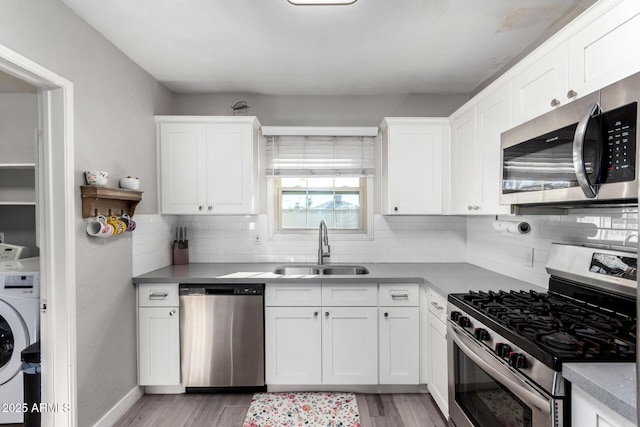 kitchen with sink, appliances with stainless steel finishes, white cabinets, washer / dryer, and light wood-type flooring