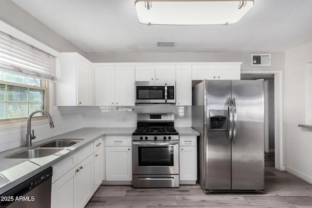 kitchen with appliances with stainless steel finishes, sink, white cabinets, decorative backsplash, and light stone countertops