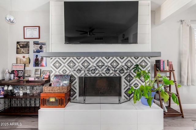 living room with a tiled fireplace, wood-type flooring, and ceiling fan