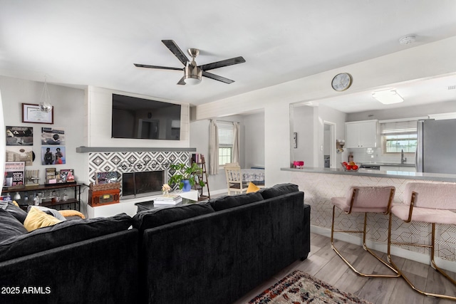 living room with a tiled fireplace, a healthy amount of sunlight, sink, and light wood-type flooring